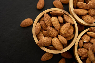 Wooden bowl with almond on black background. Top view. Flat lay (selective focus; close-up shot)