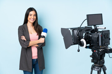 Reporter woman holding a microphone and reporting news isolated on blue background keeping the arms...