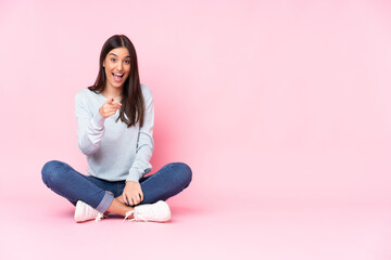 Young caucasian woman isolated on pink background surprised and pointing front