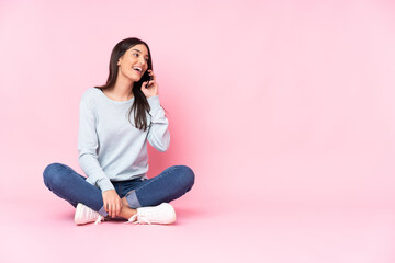 Young caucasian woman isolated on pink background keeping a conversation with the mobile phone