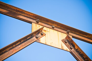 Old rusty iron structure with bolted metal profiles against a blue sky