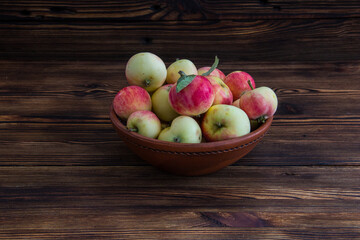 A clay bowl with apples on a wooden table.