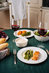 European cuisine. Salmon steak with asparagus, vegetable salad, sauce, grapes and bread with glasses of red wine. Dinner for two in the kitchen