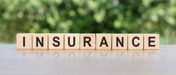 INSURANCE word written on wooden blocks. The text is written in black letters and is reflected in the mirror surface of the table. Business concept for your design.