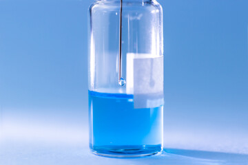 A vial with a blue vaccine with a syringe needle inside