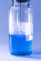A vial with a blue vaccine with a syringe needle inside