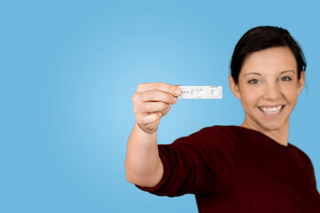 gl&uuml;ckliche junge Frau h&auml;lt negativen Covid-19 Schnelltest mit blauem Hintergrund