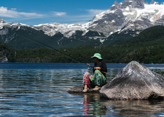 beautiful female Fisherman with green dress on top of a rock in the lake with the mountains behind