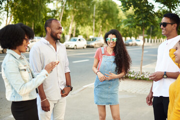 Obraz premium Young people having fun outdoors. A group of multi-ethnic friends are talking and laughing while standing in the street