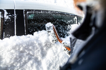 Snow clearing a car side window in winter with a brush.