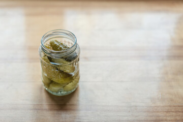 Opened glass jar with pickled cucumbers on wooden table