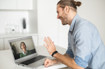 A guy waving hand, greeting with a senior woman on the laptop screen, student talking on virtual meeting with elderly female tutor, an adult son calls to mother via video call. Social distancing