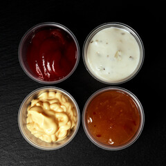 ketchup creamy cheese and sweet and sour sauces on black background top view