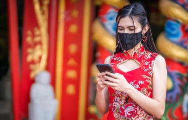 Obraz premium Asian young woman wearing red traditional Chinese cheongsam decoration and wear protective mask and smartphone for Chinese New Year Festival at shrine,Prevention of the spread of COVID-19 virus