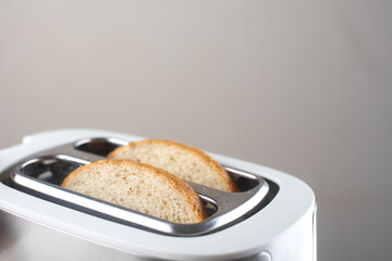 A white and silver toaster on a gray background on a white wooden table with pieces of bread sticking out