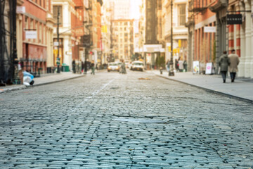 Cobblestone street with crowded intersection blurred in the sunlit background - SoHo, New York City