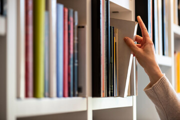 hand of woman searching for a book on shelf