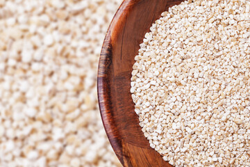Barley groats texture. Pile of uncooked grain in wooden bowl background.
