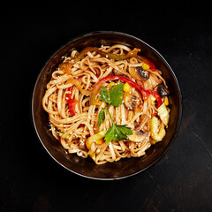wok noodles with vegetables greens and sesame seeds in a plate on a black background top view