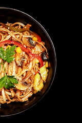 wok noodles with vegetables greens and sesame seeds in a plate on a black background top view