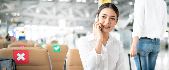 Obraz premium New normal and social distance concept.Asian young woman tourist wearing mask using smartphone searching airline flight status and sitting with distance during corona virus 2019 outbreak at airport