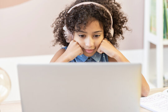 A smart curly African preteen school girl watching at laptop screen with curiosity, e-learning, distance education concept