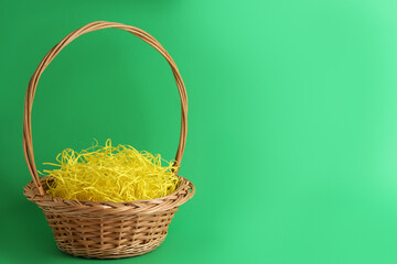 Fototapeta na wymiar Easter basket with yellow paper filler on green background, space for text