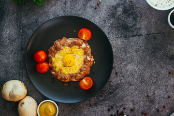 Beefsteak with egg on a plate. Delicious hot dish. The dish is decorated with cherry tomatoes and herbs. Beefsteak on a plate 