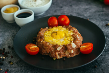Beefsteak with egg on a plate. Delicious hot dish. The dish is decorated with cherry tomatoes and herbs. Beefsteak on a plate 