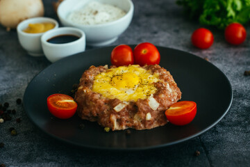 Beefsteak with egg on a plate. Delicious hot dish. The dish is decorated with cherry tomatoes and herbs. Beefsteak on a plate 