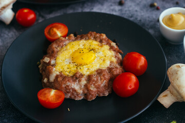 Beefsteak with egg on a plate. Delicious hot dish. The dish is decorated with cherry tomatoes and herbs. Beefsteak on a plate 