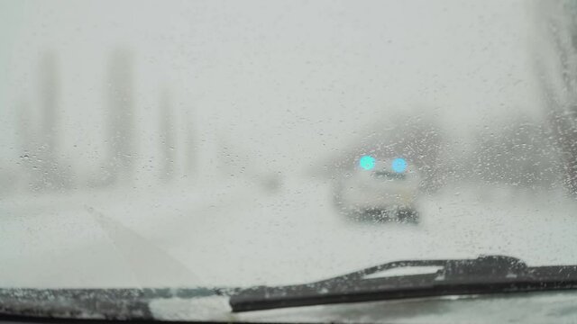 Highway with police car with siren and blinking blue lights in winter from windscreen with drops of water. Automobile in snowy frozen road