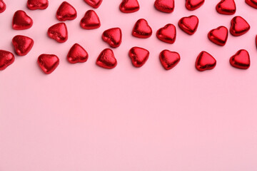 Heart shaped chocolate candies in red foil on pink background, flat lay. Space for text