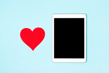 Tablet on a blue background with cute heart. The concept of meeting website, love in internet, love to your gadget and technology, love correspondence, Valentine's Day, surprise. Flat lay
