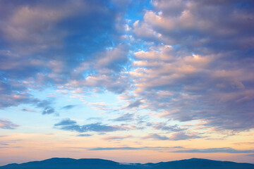 cloudscape in summer at sunrise. clouds on the blue sky in yellow and pink morning light. idyllic weather condition, picturesque scenery above the mountain ridge