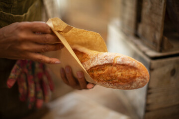 Close up female baker holding fresh baked baguette bread