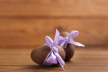 Sweet chocolate eggs with violet bows on wooden table. Space for text