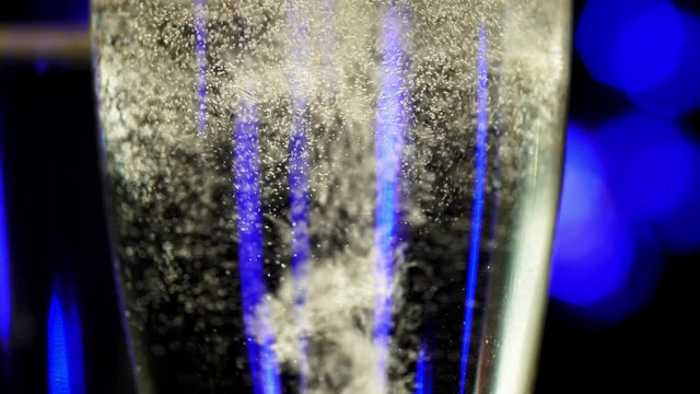 Macro view wineglasses of sparkling wine with bubbles in blue bokeh background. From bottom to top footage of closeup bocal with champagne. Elegant celebration of romantic holiday or lovely date