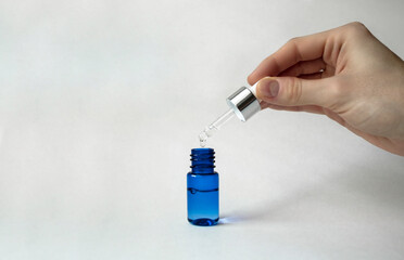 Blue glass bottle with pipette dispenser on white background. Collagen, anti-aging skin care products. Hand holds a pipette. Space for text.