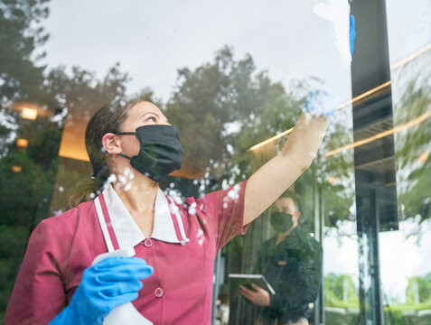 Female Hotel Maid In Face Mask Cleaning Hotel Window