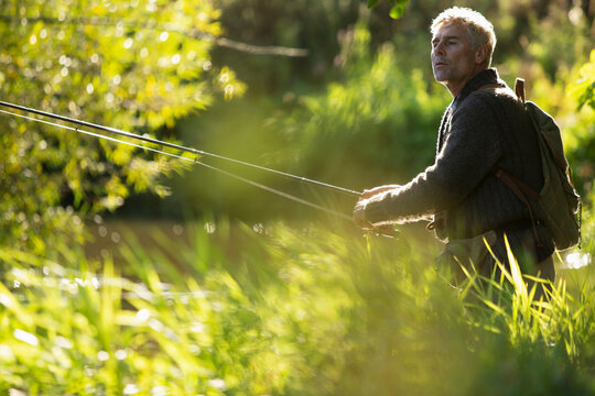 Man with backpack fly fishing with pole among sunny grass
