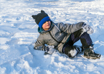 Fototapeta na wymiar Smiling caucasian boy in green jacket and blue knit cap is lying on the snow.