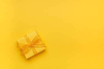 Gift box with ribbon and bow on yellow background and space for text. Top view