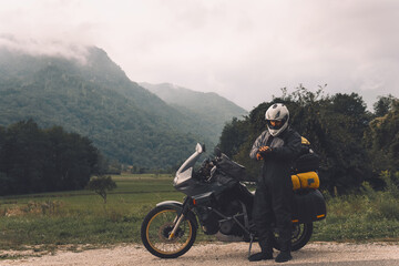 A motorcycle driver with motorbike, Adventure vacation, biker dressed in raincoat. sealed bag, water resistant, overalls. Mountains road trip, side bags equipment. copy space
