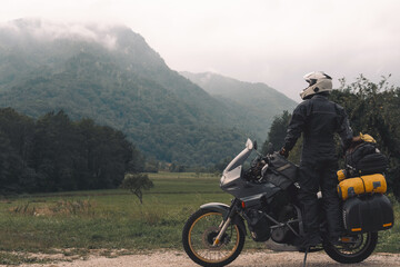 A motorcycle driver with motorbike look distance, Adventure vacation, biker dressed in raincoat. sealed bag, water resistant, overalls. Mountains road trip, side bags equipment. copy space