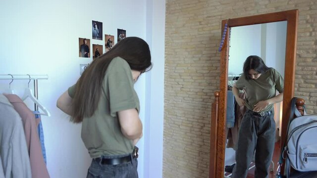 Attractive stylish woman is Looking in the  mirror. Putting together outfit &  tucking in a shirt 