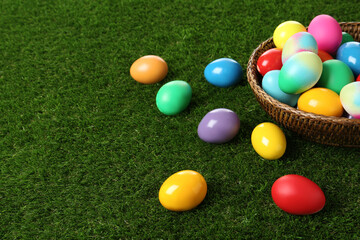 Fototapeta na wymiar Wicker basket with bright painted Easter eggs on green grass. Space for text