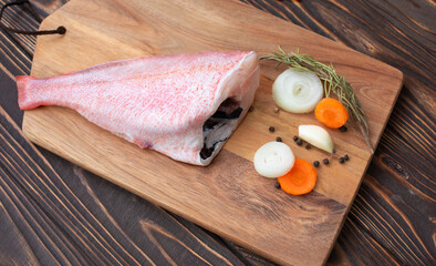 Fresh and ready to cook raw pink Perch fish with ingredients like lemon and carrot on a wooden pad, selective focus.