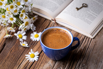 A cup of coffee with a book and daisies