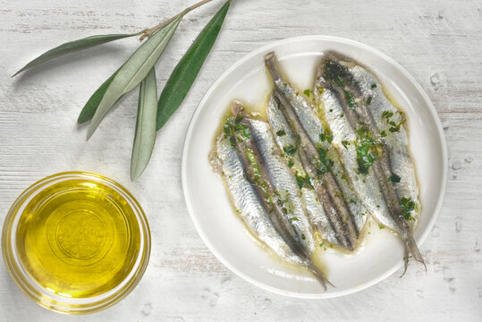 Pickled anchovies or sardines fillet in oil with herbs  and olive branch for tapas or antipasti on the white wooden background